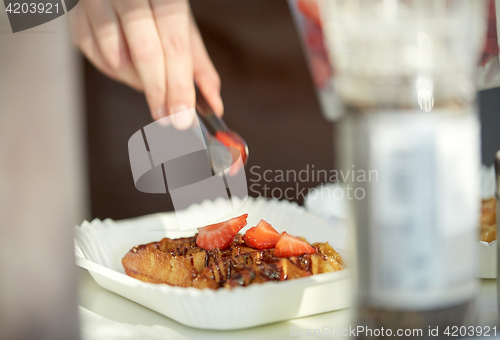 Image of close up of cook hand adding strawberry to waffle