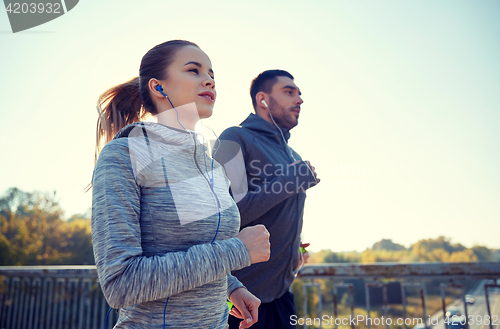 Image of happy couple with earphones running outdoors