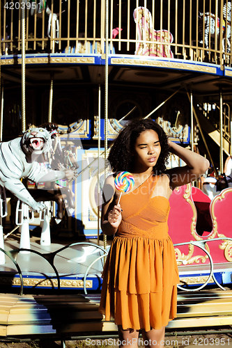 Image of cool real teenage girl with candy near carousels at amusement pa