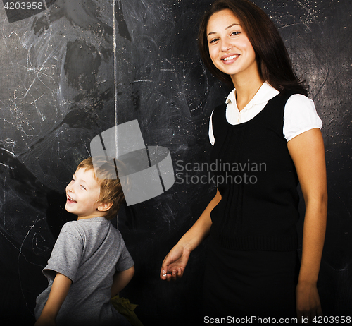 Image of little cute boy with young teacher in classroom studying at blac