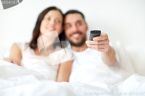 Image of happy couple lying in bed at home and watching tv