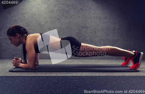 Image of woman doing plank exercise on mat in gym