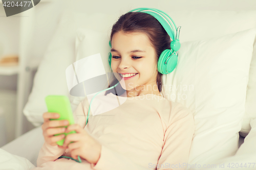 Image of happy girl lying in bed with smartphone at home