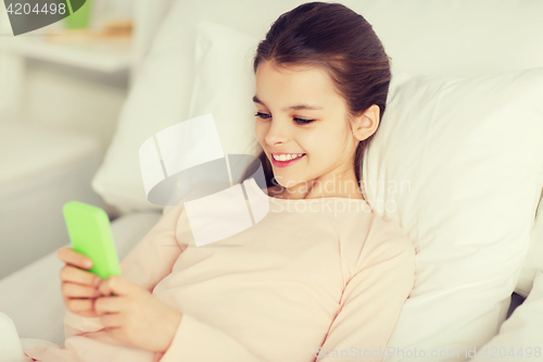 Image of happy girl lying in bed with smartphone at home