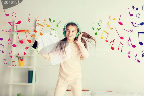 Image of girl jumping on bed with smartphone and headphones