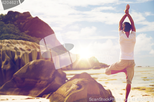 Image of man meditating in yoga tree pose over beach