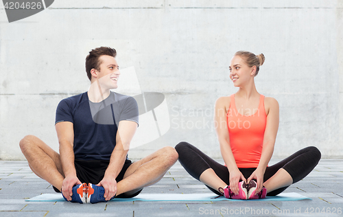 Image of happy sportive man and woman sitting on mats