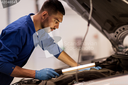 Image of mechanic man with lamp repairing car at workshop