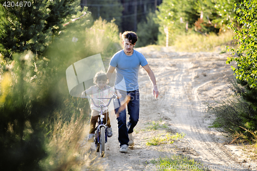 Image of father learning his son to ride on bicycle outside, real happy family in summer forest enjoing nature