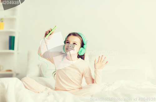 Image of girl sitting on bed with smartphone and headphones