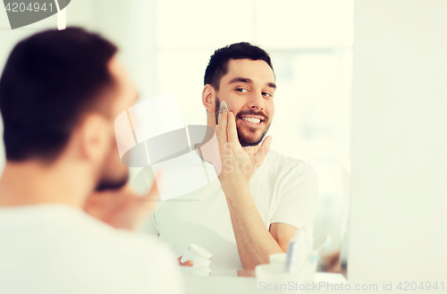 Image of happy young man applying cream to face at bathroom