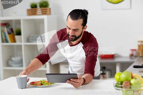 Image of man with tablet pc eating at home kitchen