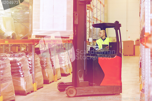 Image of man with tablet pc operating forklift at warehouse