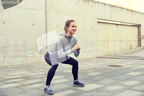 Image of happy woman doing squats and exercising outdoors