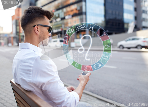 Image of man with smartphone and zodiac signs in city