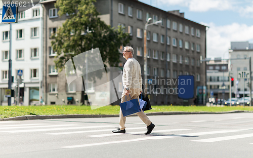 Image of senior man with shopping bags walking on crosswalk