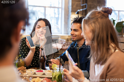 Image of friends with smartphones and food at bar or cafe