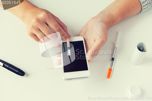 Image of close up of woman with smartphone doing blood test