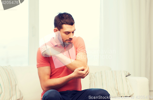 Image of unhappy man suffering from pain in hand at home