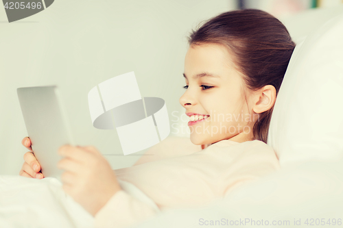 Image of happy girl lying in bed with tablet pc at home