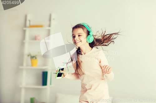 Image of girl jumping on bed with smartphone and headphones
