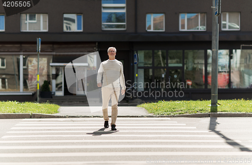 Image of senior man walking along city crosswalk