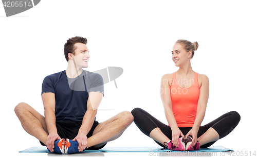 Image of happy sportive man and woman sitting on mats