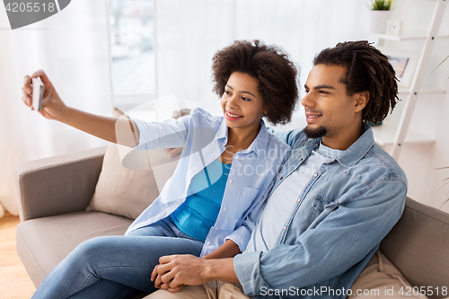 Image of happy couple with smartphone taking selfie at home