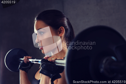 Image of young woman flexing muscles with barbell in gym