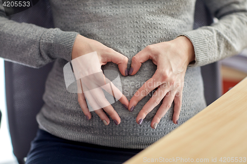 Image of pregnant woman making heart shape at office