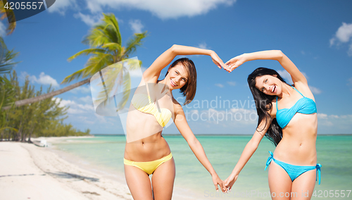 Image of happy women making heart shape on summer beach