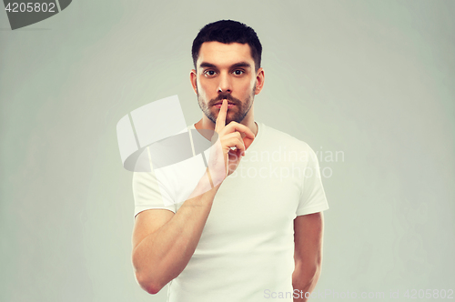 Image of young man making hush sign over gray background