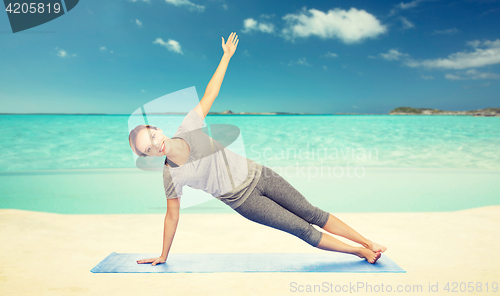 Image of woman making yoga in side plank pose on beach 