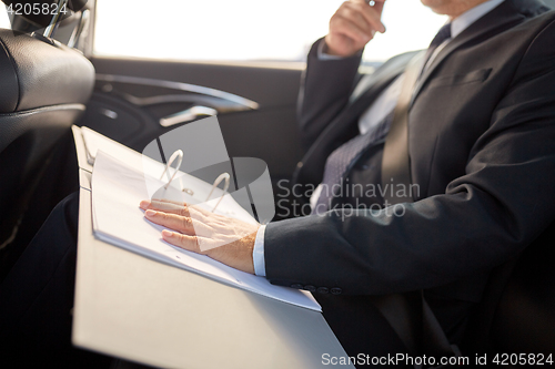 Image of senior businessman with papers driving in car