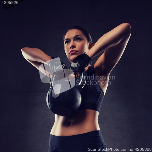 Image of young woman flexing muscles with kettlebell in gym