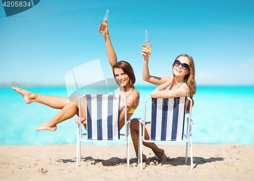 Image of happy young women with drinks sunbathing on beach