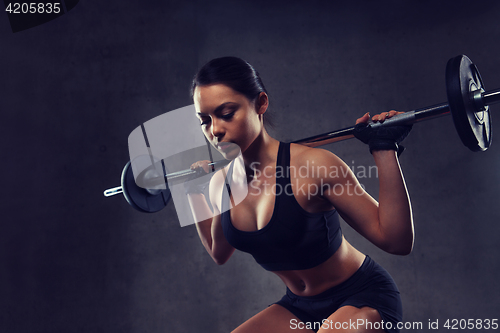 Image of young woman flexing muscles with barbell in gym