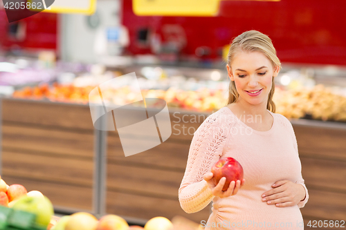 Image of happy pregnant woman with apple at grocery store