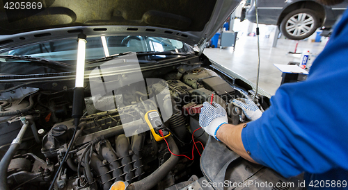 Image of auto mechanic man with multimeter testing battery