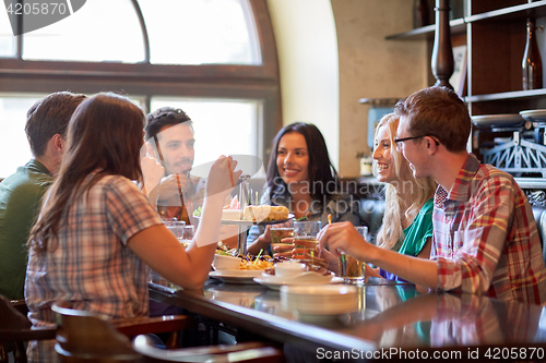 Image of happy friends eating and drinking at bar or pub