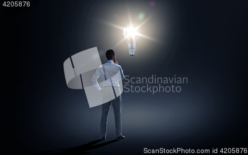 Image of businessman looking at lighting bulb over dark