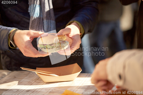 Image of hands of man eating hamburger outdoors