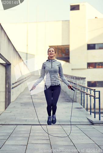 Image of happy woman exercising with jump-rope outdoors