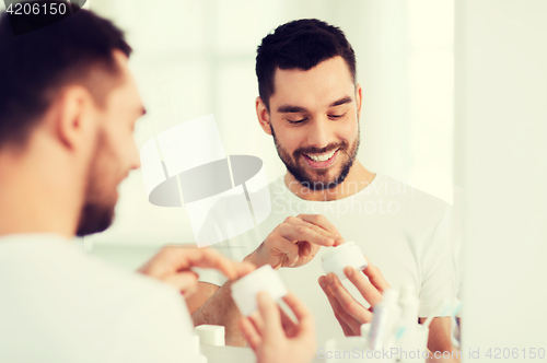 Image of happy young man applying cream to face at bathroom