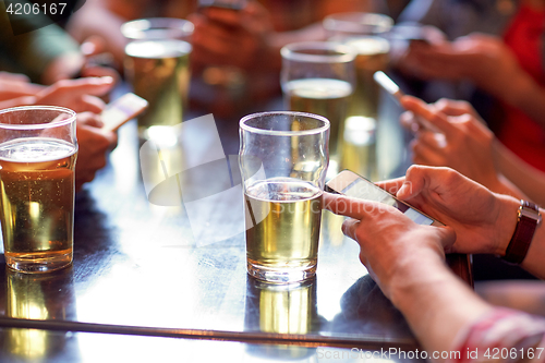 Image of friends with beer and smartphones at bar or pub