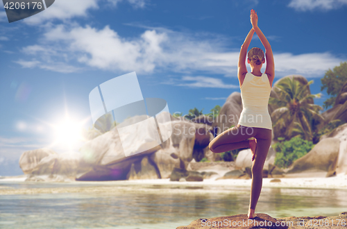 Image of woman meditating in yoga tree pose over beach