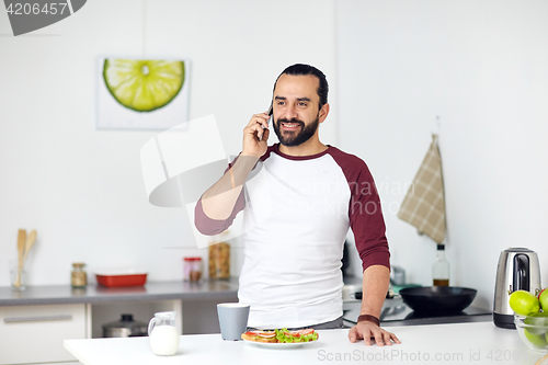 Image of man calling on smartphone and eating at home