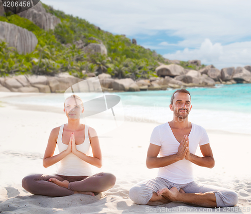 Image of smiling couple making yoga exercises on beach