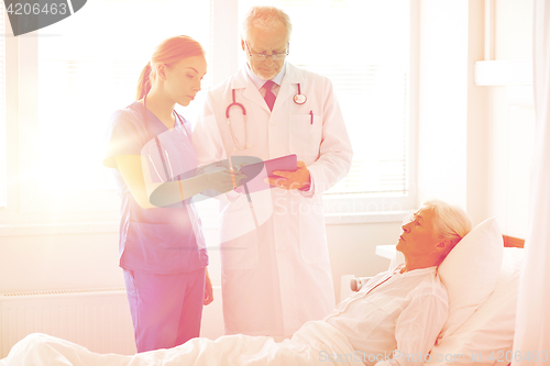 Image of doctor and nurse visiting senior woman at hospital