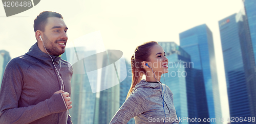 Image of happy couple with earphones running in city